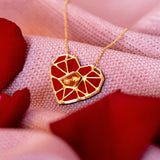 The handcrafted Fragment of Love Necklace features a heart pendant with a red, mosaic-like design, resting on soft pink fabric and surrounded by scattered red rose petals.