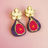 Handcrafted Fig Earrings featuring gold mirror leaves, purple outer edges, and bright pink centers, beautifully displayed on a light pink background.
