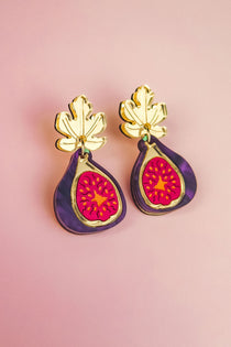 Handcrafted Fig Earrings featuring gold mirror leaves, purple outer edges, and bright pink centers, beautifully displayed on a light pink background.