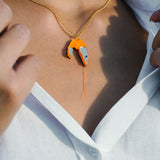 A person wearing a white shirt and a gold playful necklace with a pendant shaped like a shrimp, featuring orange and metallic colors.