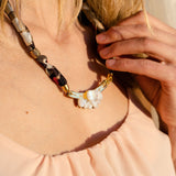 A woman in a peach sleeveless top touches a handmade necklace crafted from upcycled fabric, featuring gold accents and white beads shaped like teeth or claws.